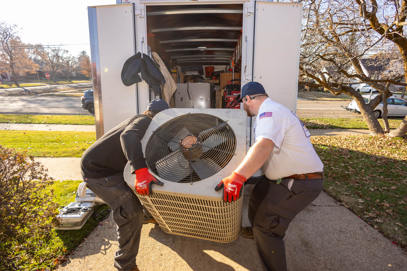
		Two Absolute Comfort employees carrying a new AC unit from a truck for an air conditioning installation.
	