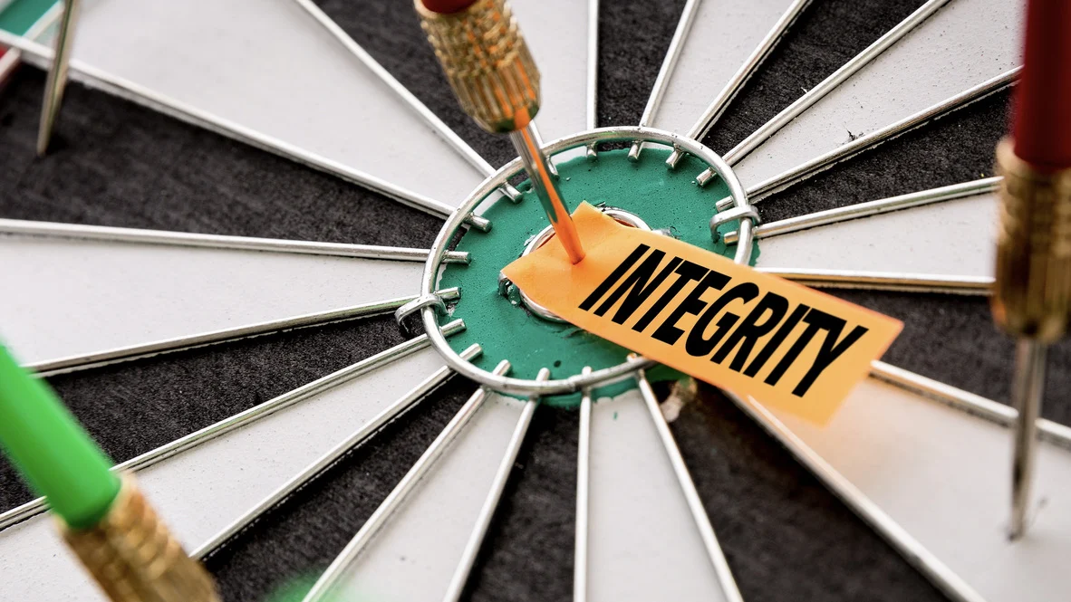 Dart board with “integrity” in bulls eye with dart through it