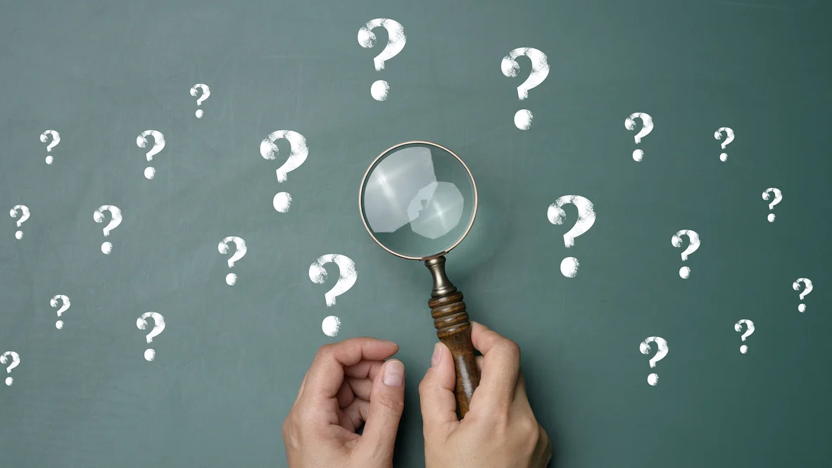 Chalkboard with drawn question marks and hand with magnifying glass